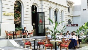 An outdoor dining area with wicker chairs and tables, a glass door entrance, and the name 'ALDO'S' on the building facade. - Beautiful Studio in Palermo Hollywood (CABA)