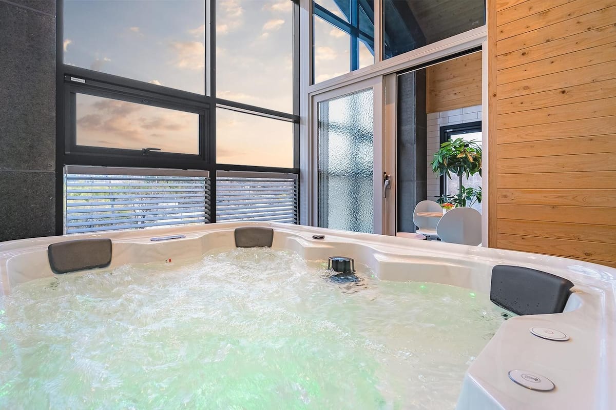 A modern bathroom with a large bathtub, large windows, and wooden paneling.