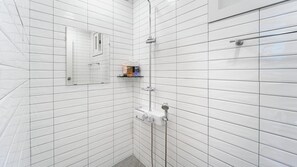 A modern bathroom with white subway tiles, a glass shower enclosure, and a small shelf with toiletries. - Gyeongju Cheongun28 Kids Poolvilla (Gyeongju)