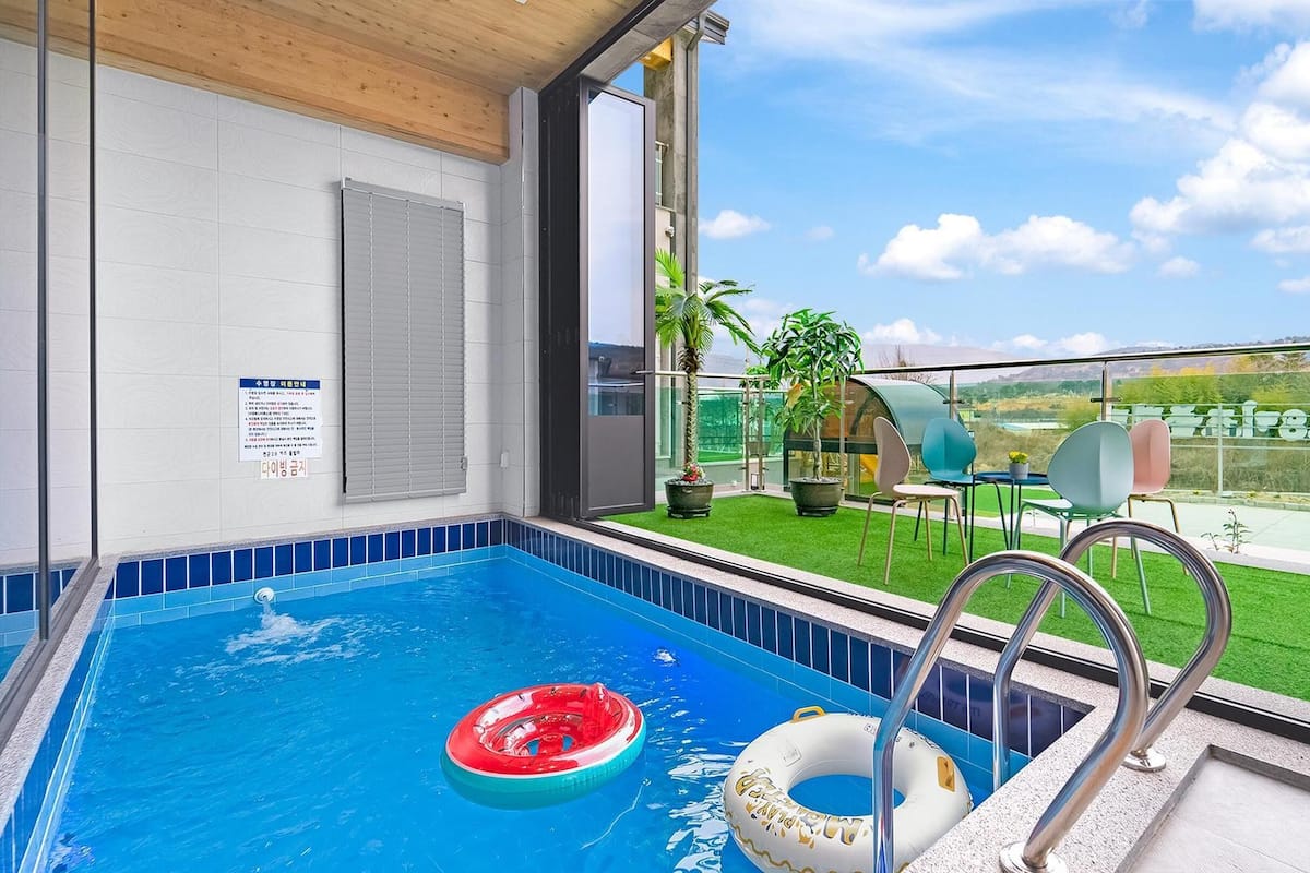 A swimming pool with two inflatable rings, a glass balustrade, and a view of a green landscape.