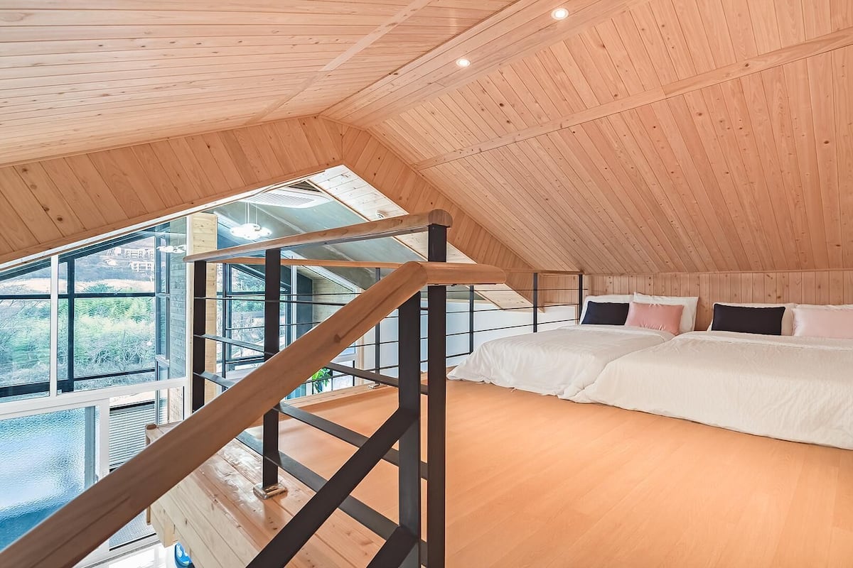 A bedroom with a large bed, wooden walls, and a view through a window.