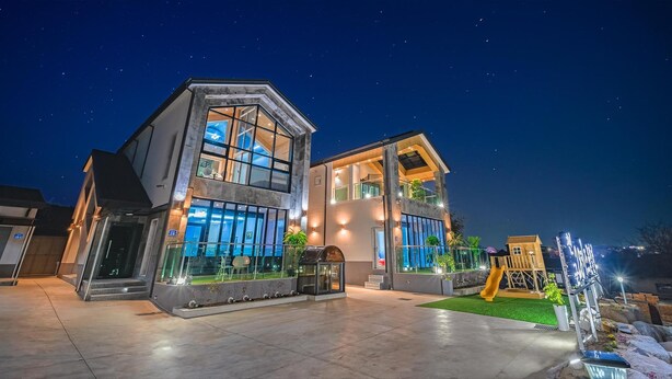 A modern two-story house with large windows and a balcony, featuring a well-lit entrance and a small outdoor play area. - Gyeongju Cheongun28 Kids Poolvilla (Gyeongju)