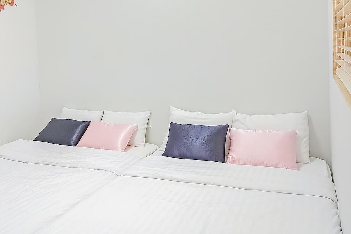 A double bed with white bedding and four pillows in various colors.