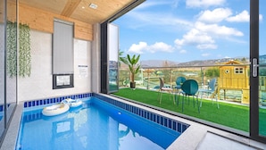 A modern indoor swimming pool with a view of a green lawn and a yellow building. - Gyeongju Cheongun28 Kids Poolvilla (Gyeongju)