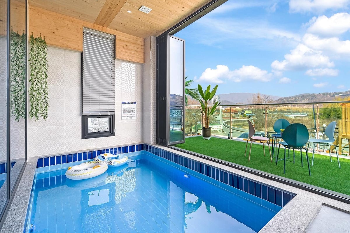 A modern indoor swimming pool with a view of a green lawn and a yellow building.