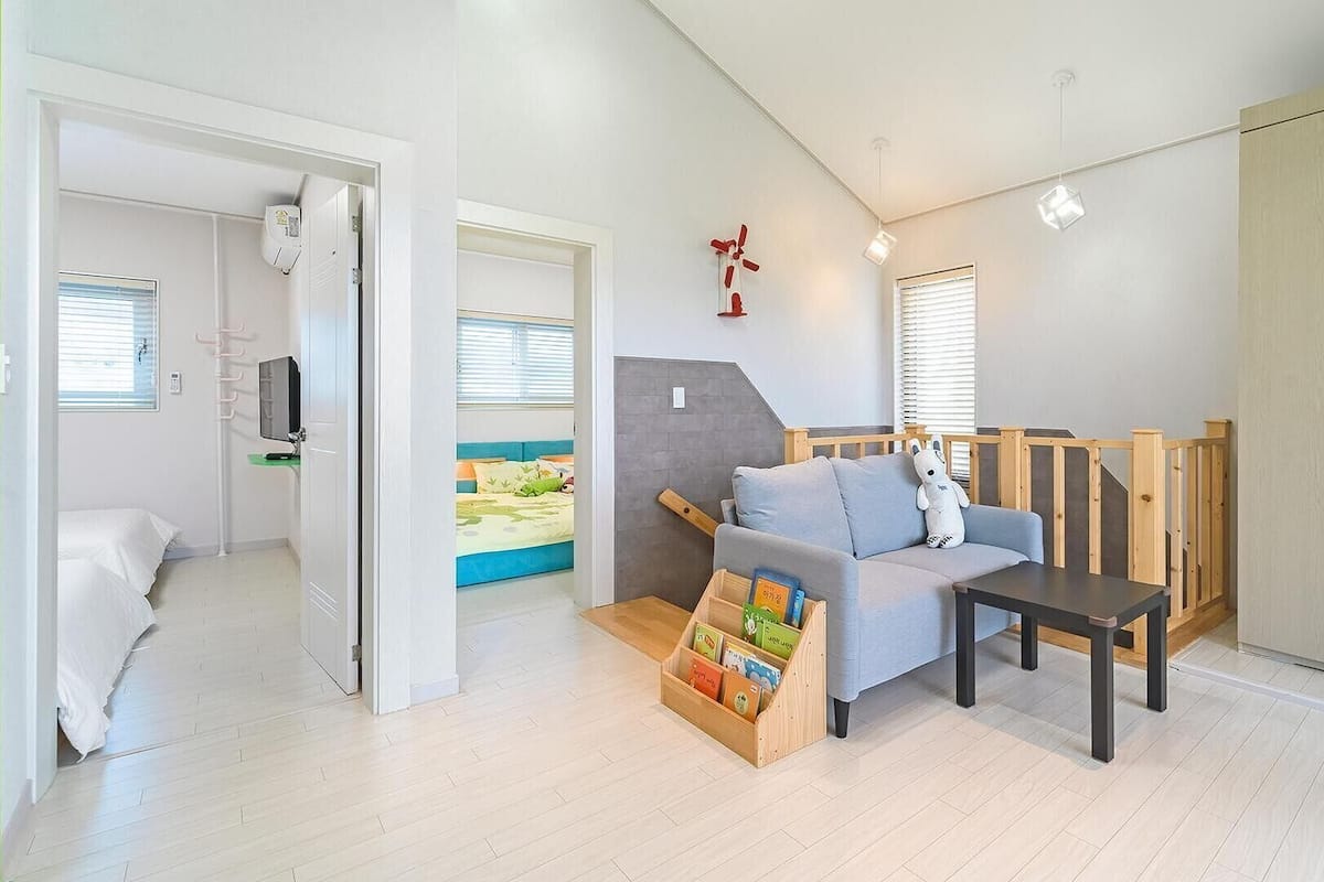 A modern, well-lit room with a sofa, a small table, a bookshelf, and a staircase leading to another level.