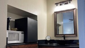 Un baño con lavamanos blanco, espejo, microondas y tocador de madera oscura.