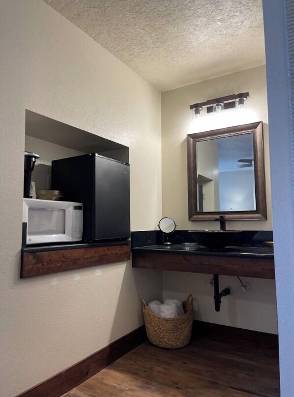 A bathroom with a white sink, a mirror, a microwave, and a dark wooden vanity.