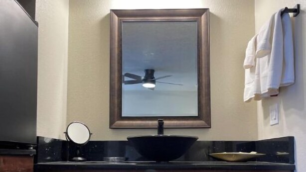Un baño con tocador de madera oscura, un lavabo negro, un espejo y un perchero para toallas.