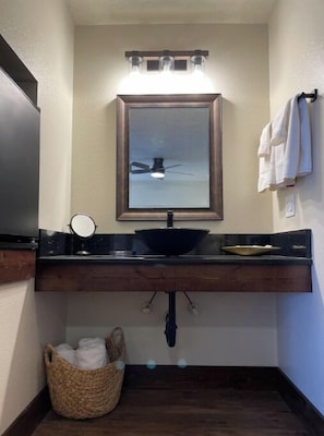 Une salle de bain avec un meuble-lavabo en bois foncé, un lavabo noir, un miroir et un porte-serviettes.