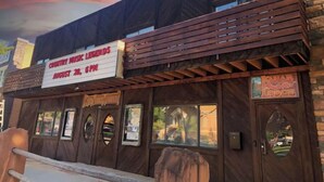 Un edificio con fachada de madera rústica, un cartel anunciando el evento 'Country Music Legends' el 28 de agosto a las 6 PM, y un letrero que dice 'Knap Lodge'.