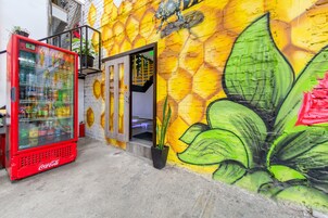 A red Coca-Cola refrigerator, a potted plant, and a vibrant mural with large green leaves.