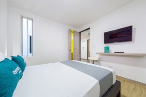 Habitación de hotel con cama, televisión montada en la pared, una mesita y una ventana.