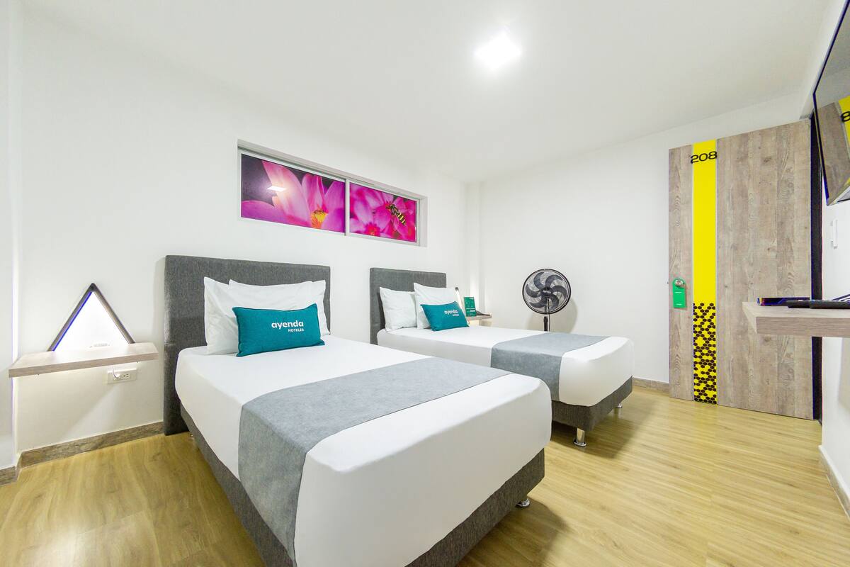 A hotel room with two beds, a ceiling fan, a wooden door, and a wall-mounted TV.