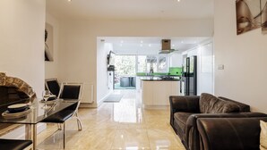 A modern kitchen with a green stove, a dining area with a glass table and black chairs, and a leather sofa. - Luxury Town House (Bolton)