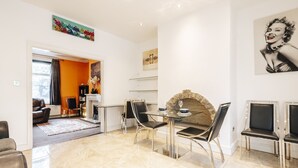 A modern living room with a fireplace, a dining area with a glass table and chairs, and a hallway leading to another room. - Luxury Town House (Bolton)