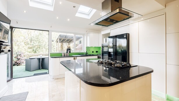 A modern kitchen with a central island, built-in appliances, and a large window overlooking a garden. - Luxury Town House (Bolton)