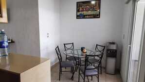 A dining area with a round table, six chairs, a painting above the table, a water dispenser, and a refrigerator.