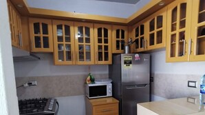 A compact kitchen with wooden cabinets, a microwave, a refrigerator, and a gas stove.