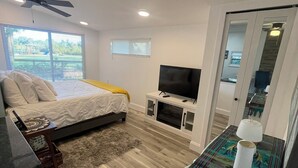 A bedroom with a bed, a TV, a ceiling fan, and a window.