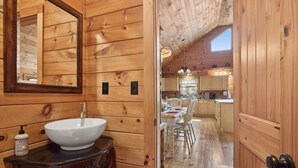 A wooden cabin interior with a wooden sink, a mirror, and a dining area with a table and chairs.
