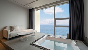 Un baño moderno con bañera, un sofá y un ventanal con vistas al mar.