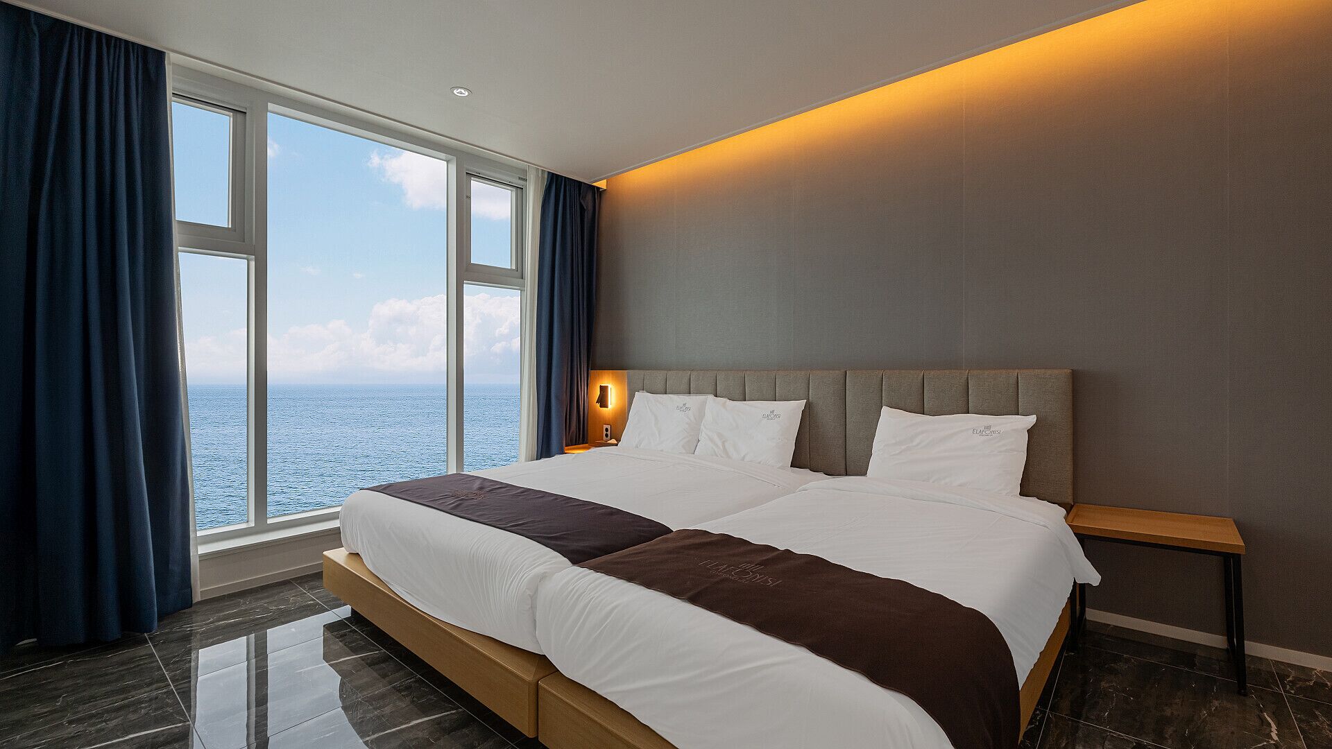 Una cama grande con vista al mar, una mesita de noche y una lámpara de pared.