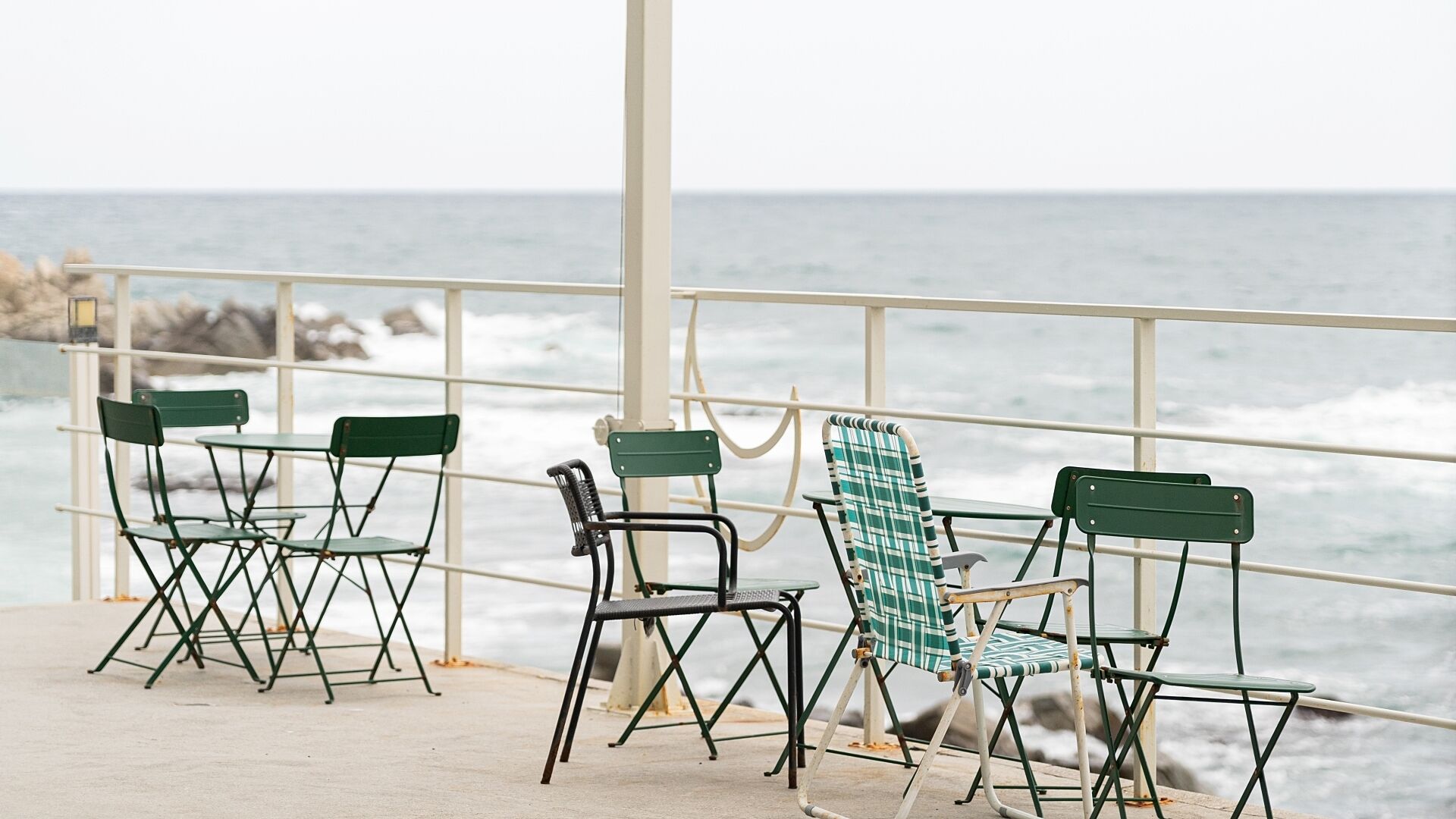 A covered outdoor seating area with metal chairs and tables, overlooking the ocean.