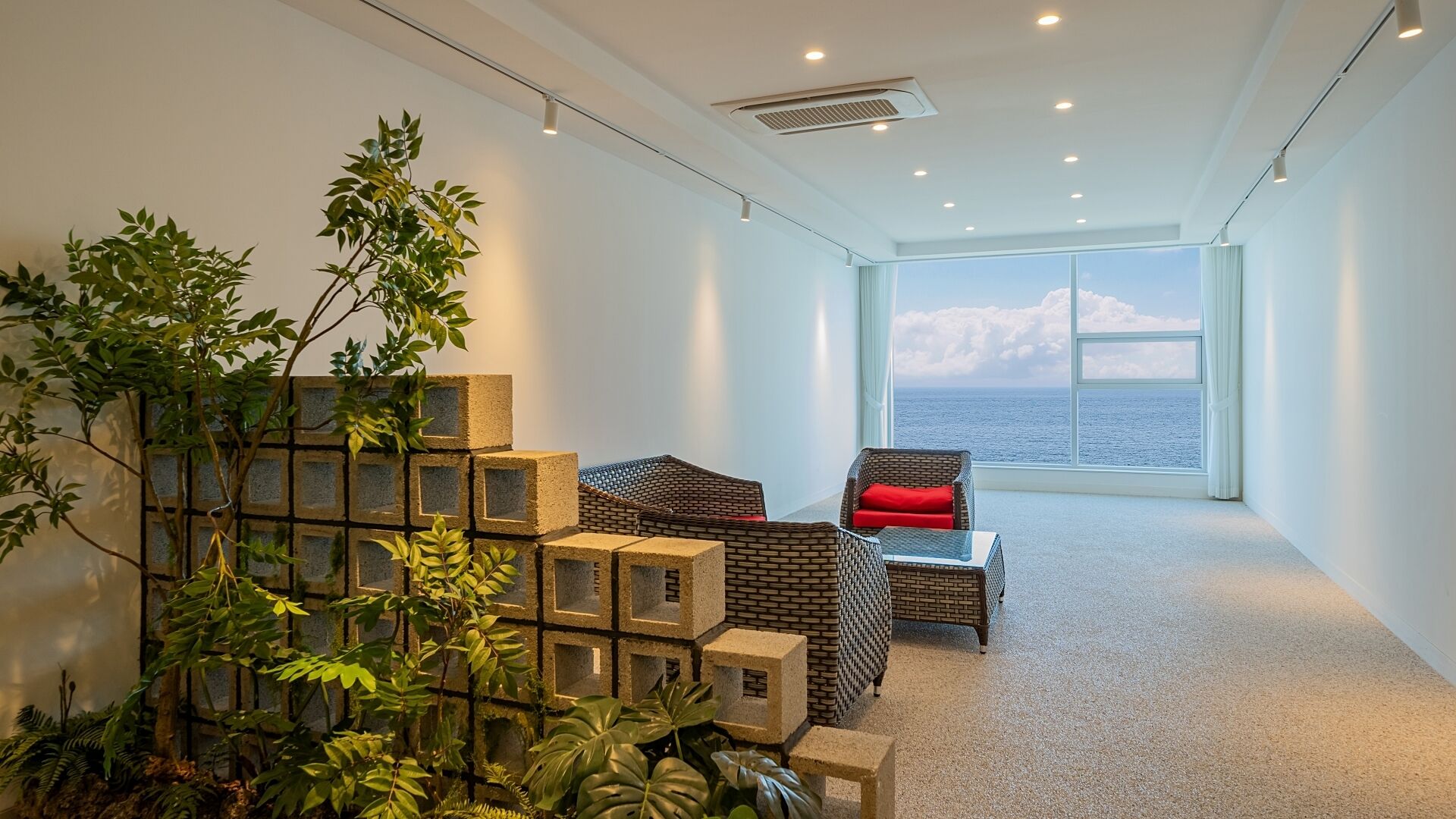 A modern interior with a seating area, a large window with a view of the sea, and a decorative plant arrangement.