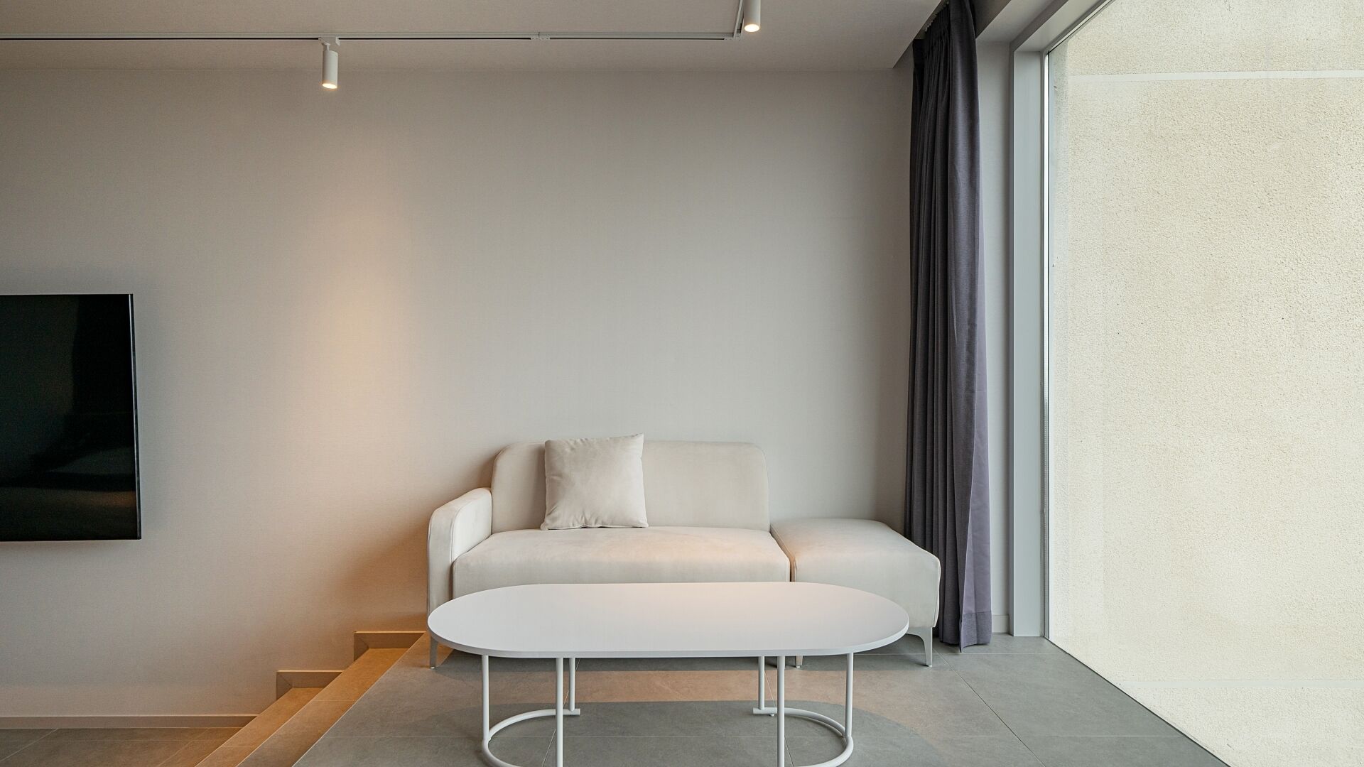 A modern living room with a white sofa, a round coffee table, and a large window with curtains.