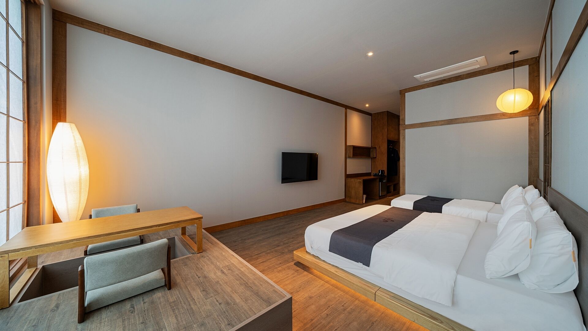 Una habitación de hotel con cama, escritorio, silla, televisor y un ventanal grande.