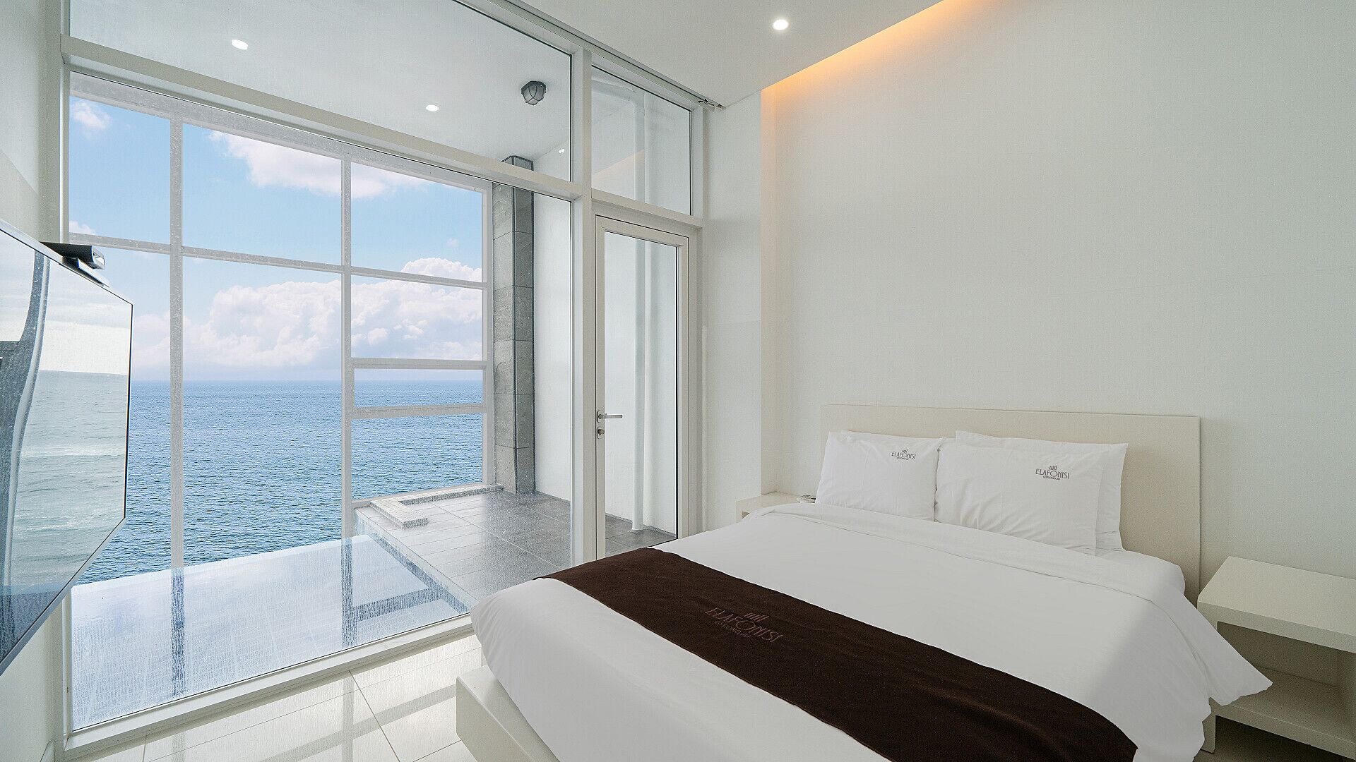 Ein modernes Schlafzimmer mit einem großen Bett, Meerblick durch raumhohe Fenster und einem Balkon.