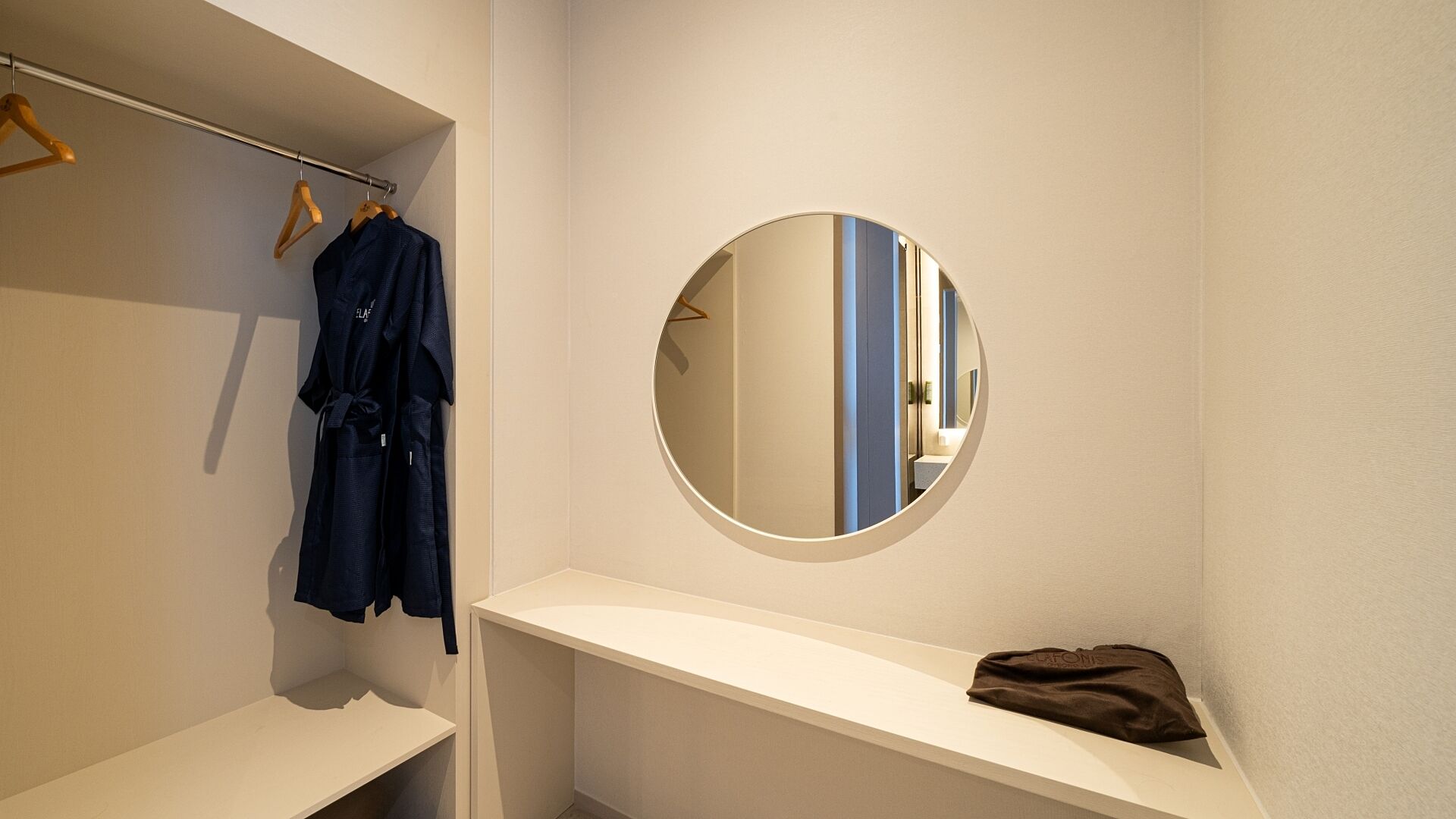 A bathroom with a mirror, a robe hanging on a rack, and a shelf with a bag.