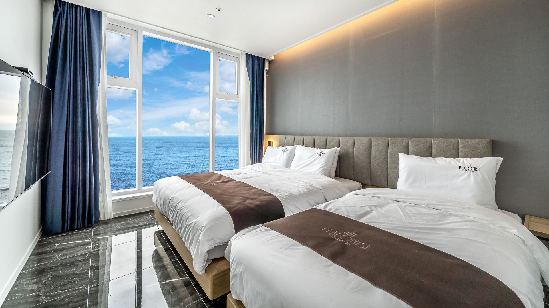 A hotel room with two beds, a large window with a view of the sea, and a modern design.