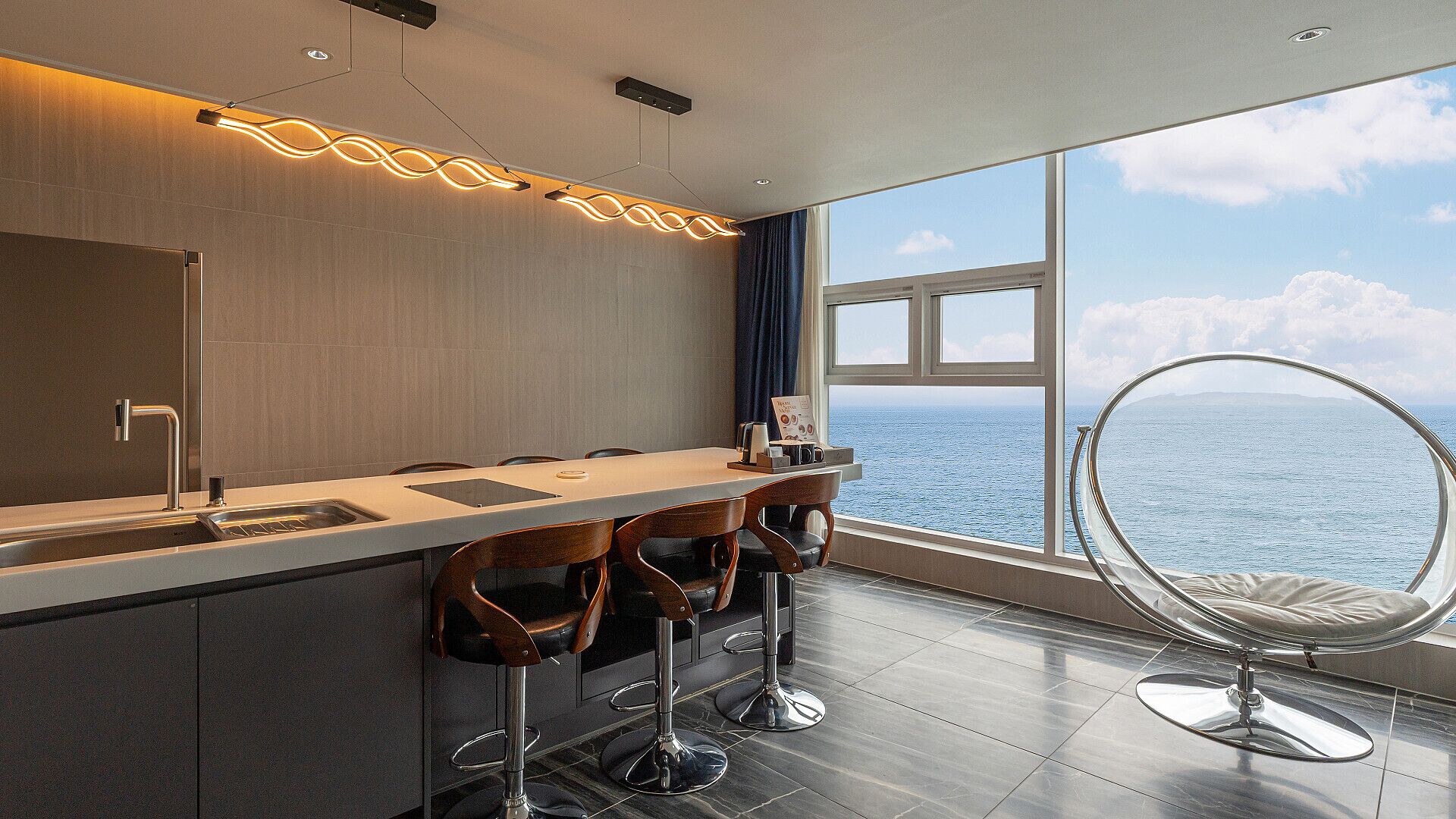 A modern kitchen with a large window, a bar area with stools, and a unique circular chair.