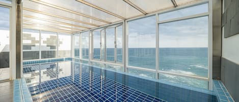 Une piscine intérieure moderne dotée de grandes baies vitrées offrant une vue sur l’océan.