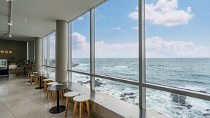 Un interior moderno con amplios ventanales con vistas al océano, que incluye una zona de estar con mesas y sillas.