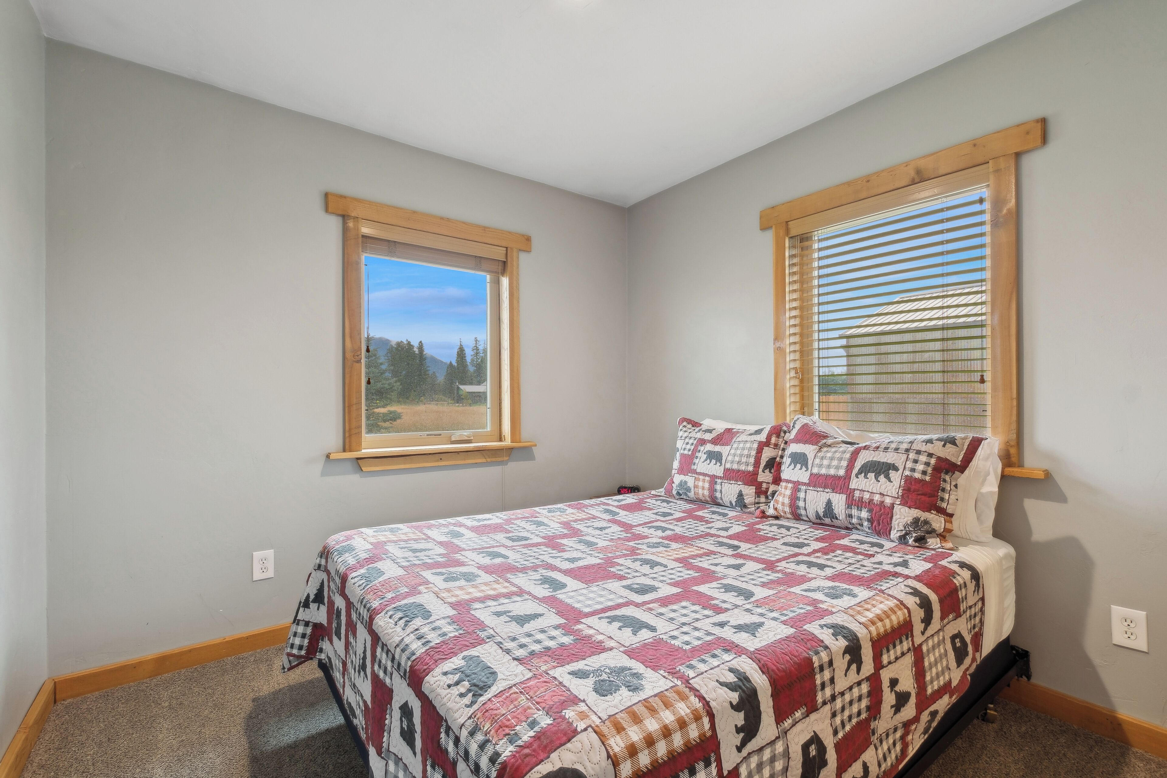 A bedroom with a bed, two windows, and a view of trees.