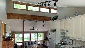 A kitchen with white cabinets, a microwave, a refrigerator, and a dining area with a table and chairs. - Lake Simcoe Getaway — Just 1 Hour from Toronto! Family cottage rarely offered! (Georgina)