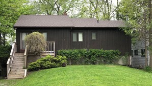 A two-story house with a front porch, a small garden, and a wooden fence. - Lake Simcoe Getaway — Just 1 Hour from Toronto! Family cottage rarely offered! (Georgina)