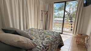 Une chambre avec un lit, une petite table ronde et une vue sur l’extérieur grâce à une porte-fenêtre coulissante.