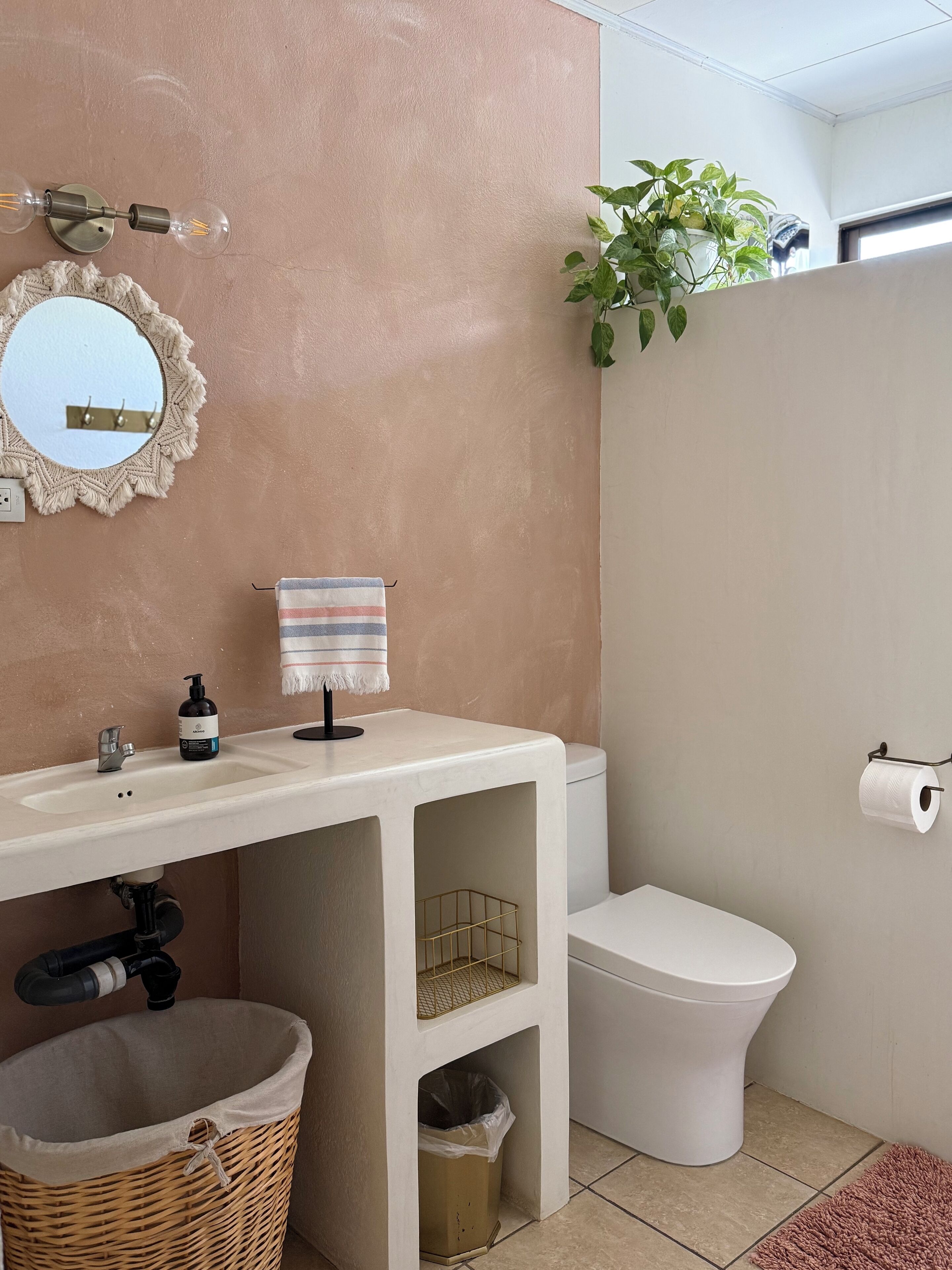 Un baño con lavamanos, espejo, toalla, inodoro y una planta.