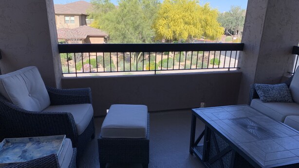 Un balcone con mobili in vimini, un tavolino e vista su una zona residenziale con alberi e case.