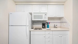 A compact kitchen with white cabinetry, a built-in microwave, a refrigerator, and a coffee maker. - A breathtaking oceanfront studio w/ a private balcony (Daytona Beach)