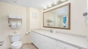 A bathroom with a toilet, a sink, a mirror, and a towel rack. - A breathtaking oceanfront studio w/ a private balcony (Daytona Beach)
