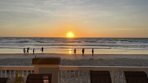 A beach scene with a sunset, ocean waves, and people walking along the shore. - A breathtaking oceanfront studio w/ a private balcony (Daytona Beach)