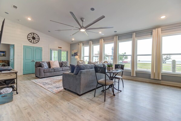A spacious living room with a ceiling fan, large windows, and a cozy seating area.