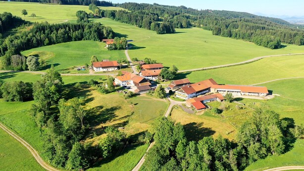 Vista aérea de una propiedad rural con varias construcciones, rodeada de campos verdes y bosques.