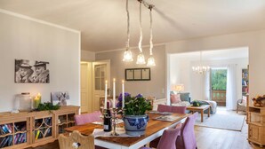 Un comedor con una mesa de madera, sillas moradas, un florero con flores y una estantería.
