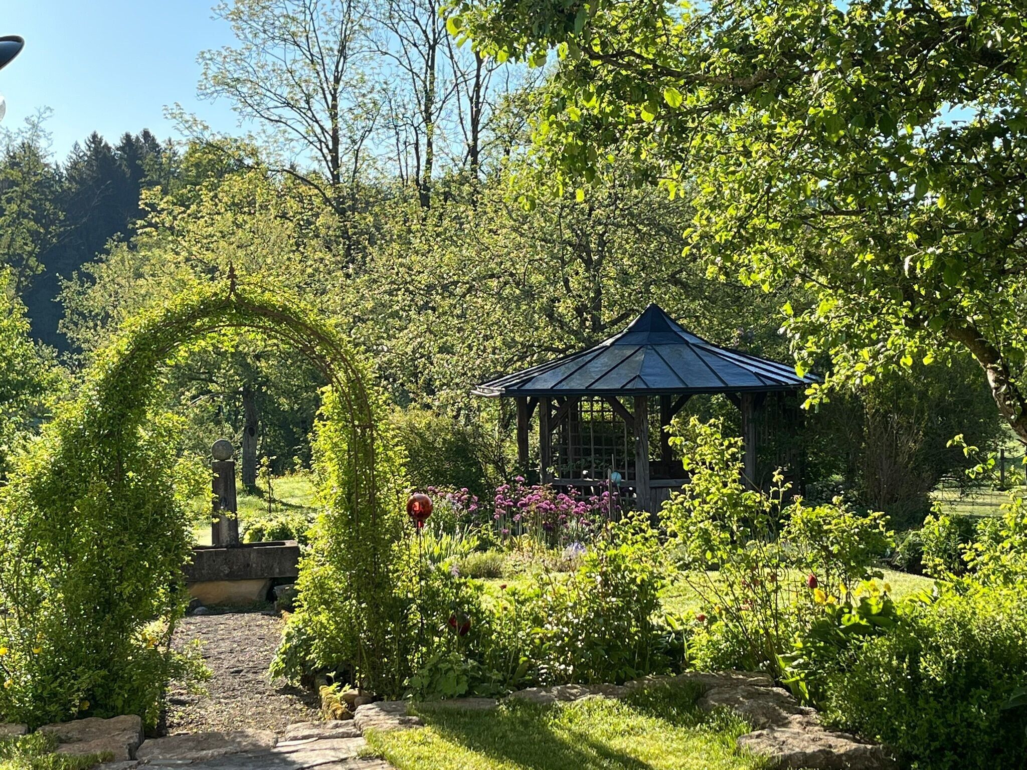 Un jardin agrémenté d’un belvédère, d’un chemin de pierres et d’une végétation luxuriante.